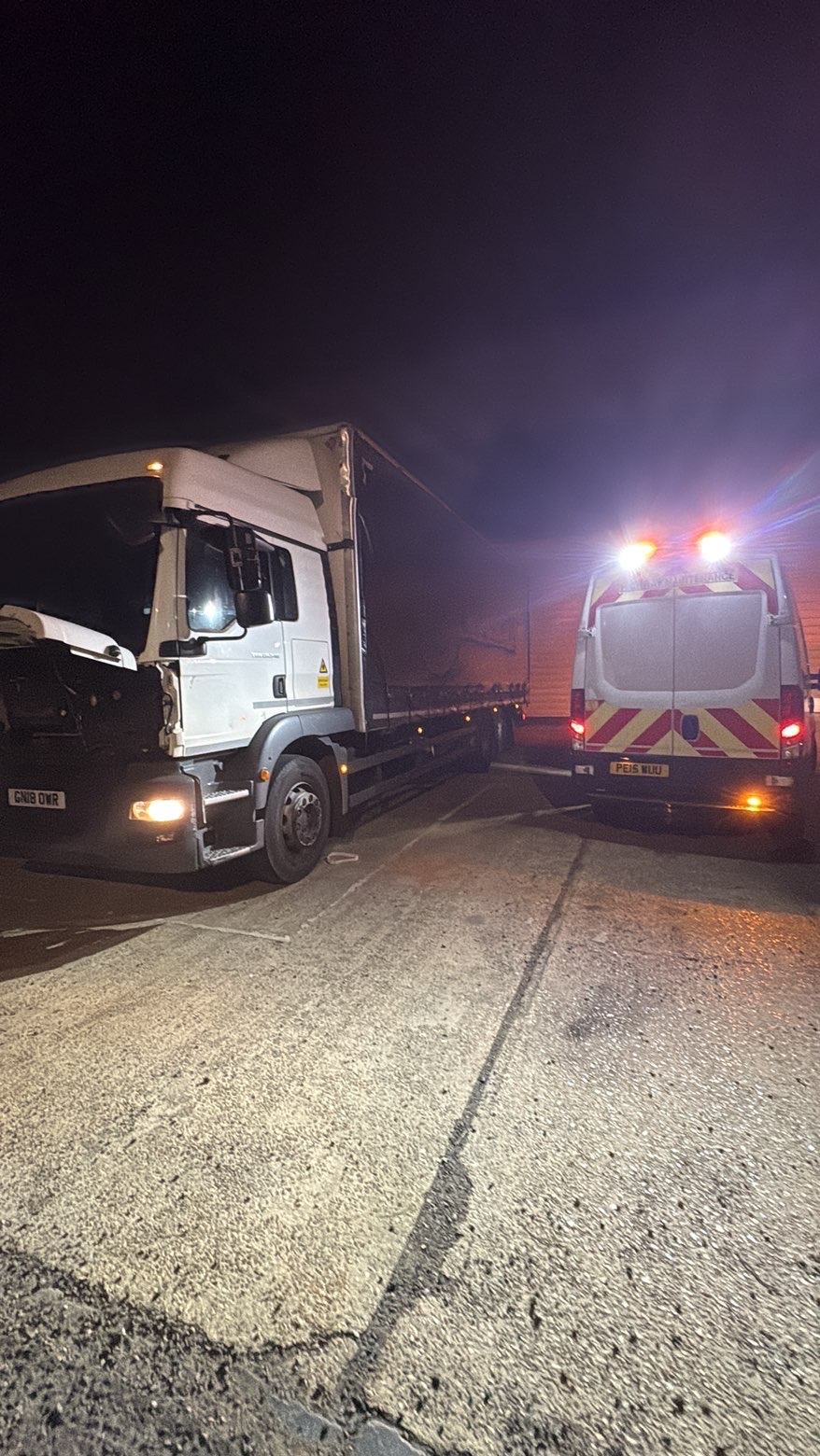 Curtainside lorry with the cab open beside a service van at night