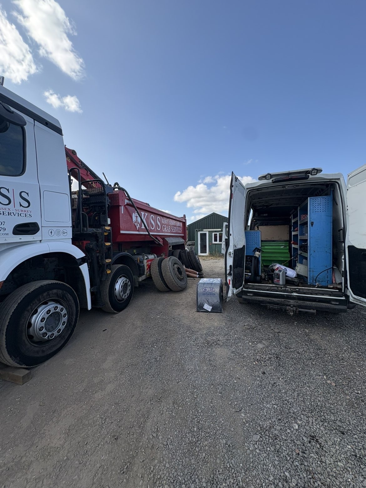 Tipper grab lorry on timber blocks with wheels off beside the service van