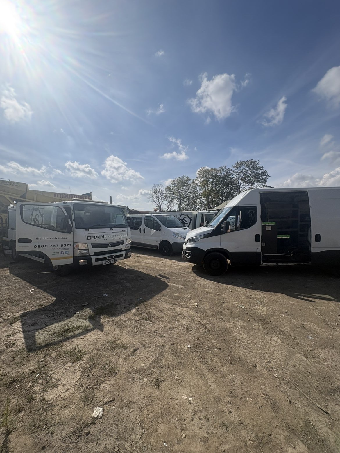 Line of commercial vans and a tipper truck in a yard on a sunny day